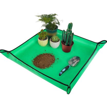 Green repotting mat with corners snapped up, holding potted plants, loose soil and a trowel (plants and tools not included)
